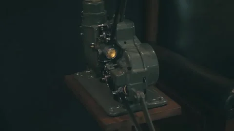 In the semi-darkness next to a leather chair, old movie projector shows a film Stock Footage 323907267