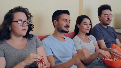Semi-profile side shot of four friends eating popcorn and watching TV show Stock Footage 93874476