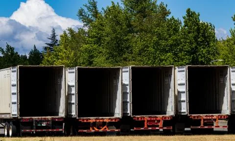 Semi tractor trailers empty and open parked in a lot with trees Stock Photos