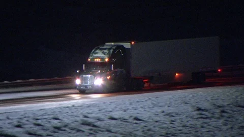 Semi truck drives down freeway covered in snow at night (long distance pan) Stock Footage