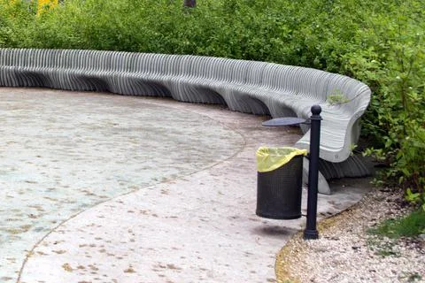 Semicircular extended bench of curly vertical elements and black metal trash can Stock Photos