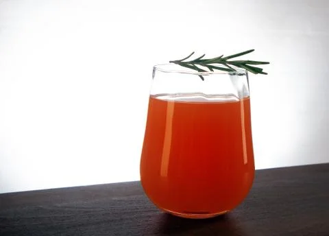 Semicircular glass of fresh orange juice with rosemary sprig on top Stock Photos