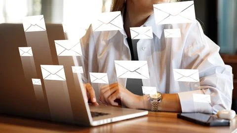 Sending and receiving emails while working on a laptop in a busy office setting Stock Photos