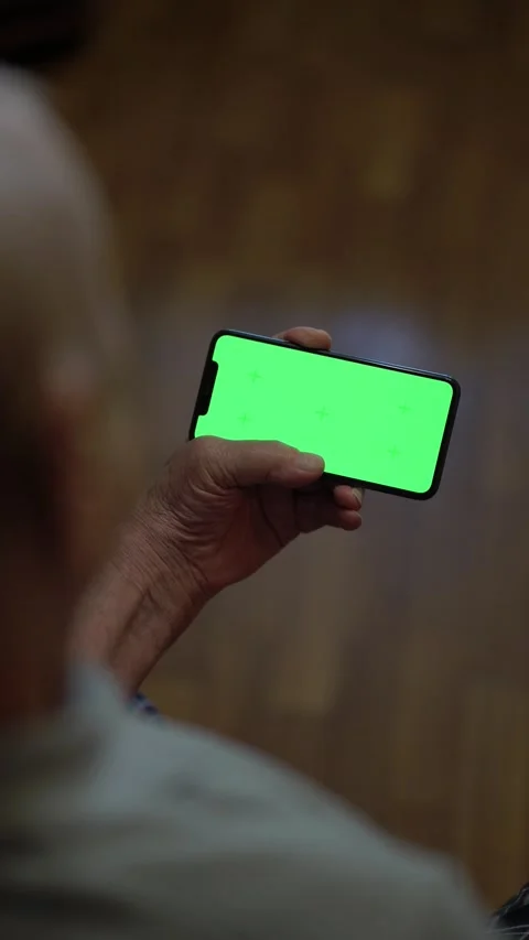 Senior 80-year-old views information or news on chroma key phone screen indoors Stock Footage 346176396