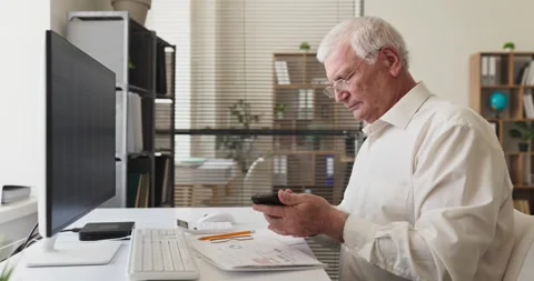 Senior accountant checking smartphone at desk, computer and financial documents Stock Footage 341903549