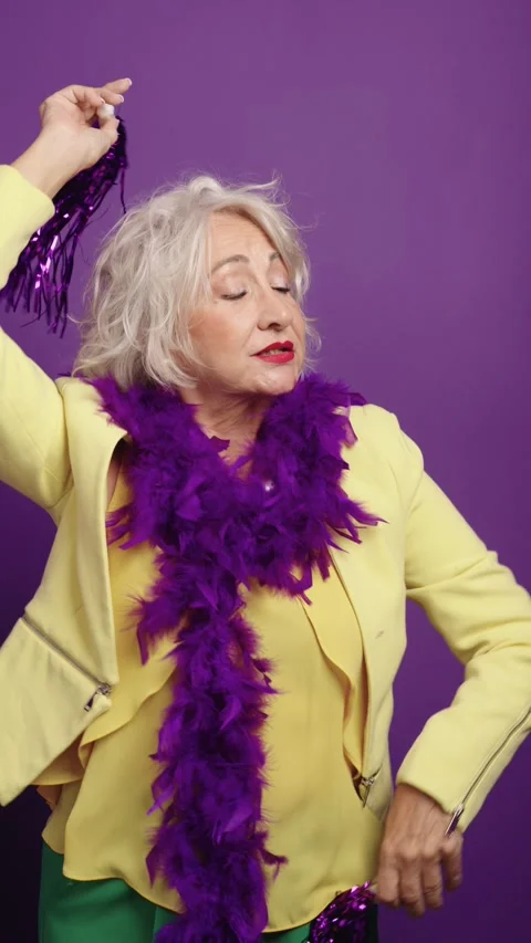 Senior actress posing with purple feather boa on solid background Stock Footage 290173535