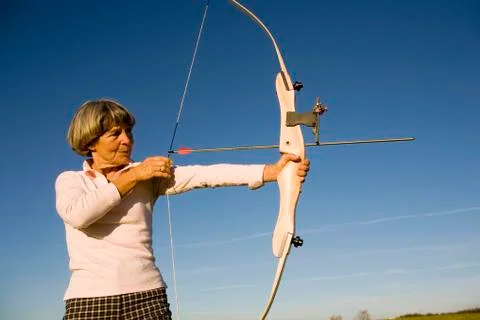 Senior adult woman using bow and arrow, side view Stock Photos