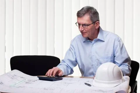 Senior architect or engineer calculating a project in an white office Stock Photos