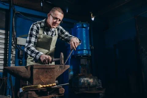 Senior an artisan blacksmith knocks with a hammer on iron to shape Stock Photos