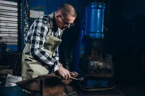 Senior an artisan blacksmith knocks with a hammer on iron to shape Stock Photos