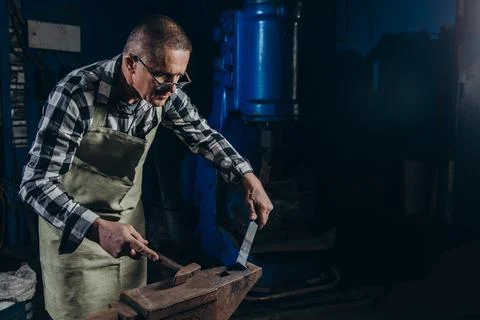 Senior an artisan blacksmith knocks with a hammer on iron to shape Foto stock