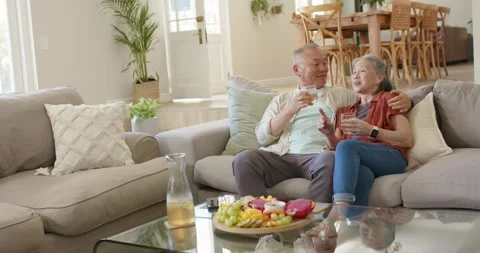 Senior Asian couple sitting on sofa, man raising glass sparking conversation Stock Footage 342392780
