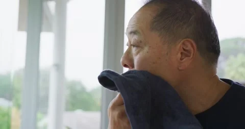 Senior Asian man lifting dark blue towel, wiping, patting face to dry on porch, Stock Footage 337745333