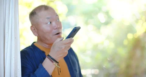 Senior Asian man responding to call, holding phone at doorway orange tee and Stock Footage 342494828