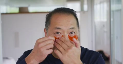 Senior Asian man seeing single orange patch, peeling second backing, aligning Stock Footage 337745349
