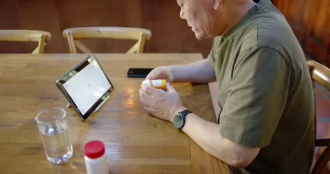 Senior Asian man sitting at dining table consulting tablet on stand checking Stock Footage 336658815