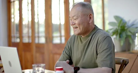 Senior Asian man sitting at dining table leaning to laptop speaking gesturing Stock Footage 343100734