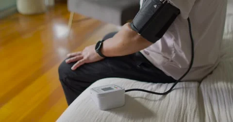 Senior Asian man sitting on sofa cuff inflating, monitor recording blood Stock Footage 337730627