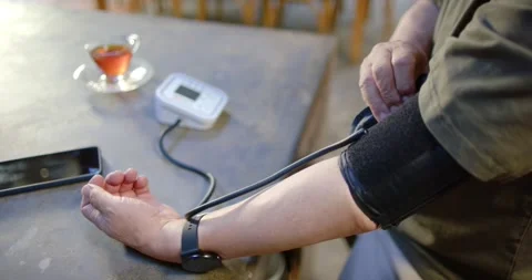 Senior Asian man sitting at table preparing blood pressure reading, placing cuff Stock Footage 337933453