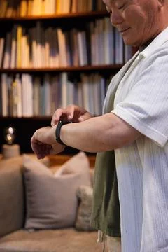 Senior Asian man standing in study by bookshelf wearing tee and adjusting Foto stock