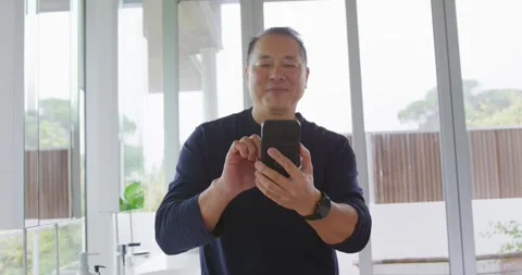 Senior Asian man standing at vanity area wearing dark sweater and smartwatch, Stock Footage 337745372