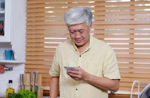 Senior asian man using smart phone while standing in kitchen at home, people Foto stock