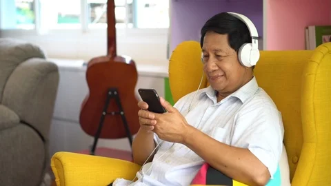 Senior asian man using smartphone listening music with headphones on sofa Stock Footage 110917713