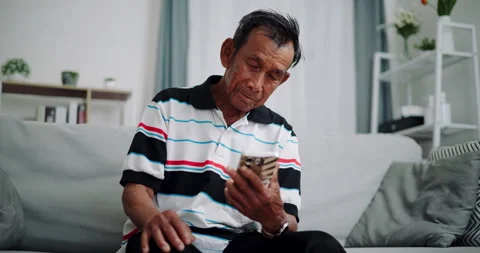 Senior Asian man using smartphone on sofa in living room at home. Vidéo 315861657