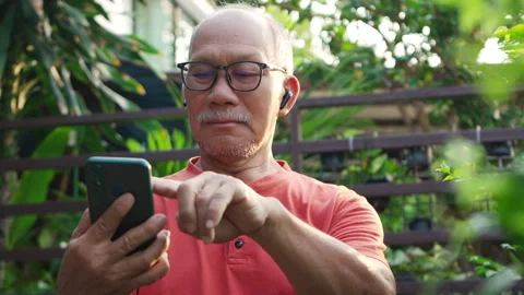 Senior Asian Man Using Smartphone and earphones in Garden, Engaged and Happy Stock Footage 321927437