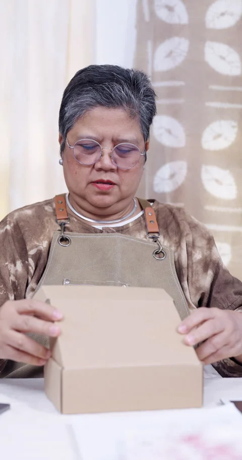 Senior asian retired artisan opens carton flaps, checks online order list, Stock Footage 335367110