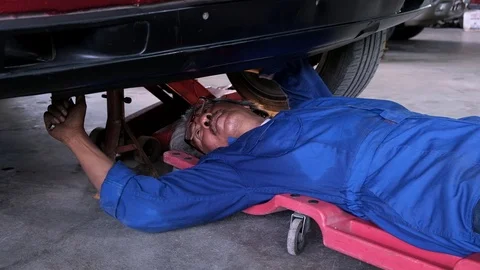 Senior auto mechanic checking screw under engine car in garage Stock Footage 119165406