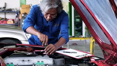 Senior auto mechanic using screwdriver tighten and check oil level of car engine Stock Footage 119418863