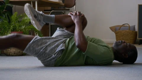 Senior Black Man Doing Glute Stretch Exercise on Floor at Home Stock Footage 315450342