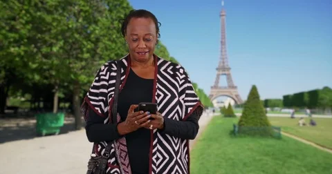 Senior black woman using her cellphone in Paris waves to someone off camera Stock Footage 85318534
