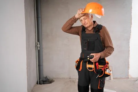 Senior builder man in uniform with hard hat standing in repairing house, tire Stock Photos