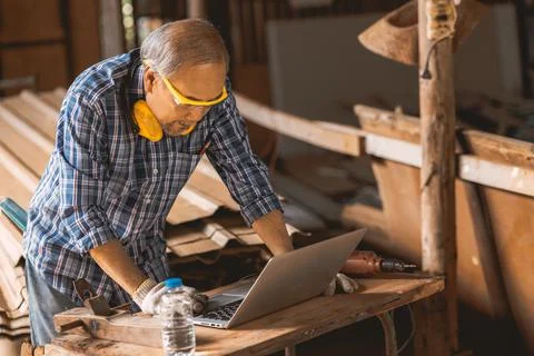 Senior builder wood worker using laptop computer at aiding design at construc Stock Photos