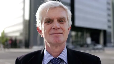 Senior business man looking at camera outside with office buildings in backgroun Stock Footage 229640754