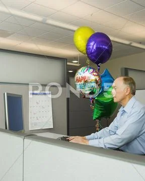 Senior businessman in a cubicle with a bunch of retirement balloons Stock Photos