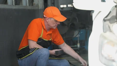 Senior car mechanic checking tire pressure in garage . old Auto mechanic Stock Footage 246989160