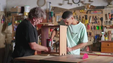 Senior Carpenter and Young Apprentice Collaborating in Carpentry Workshop Foto stock