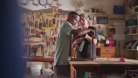 Senior carpenter being assisted by his apprentice, candid carpentry scene o.. Video stock 246845894