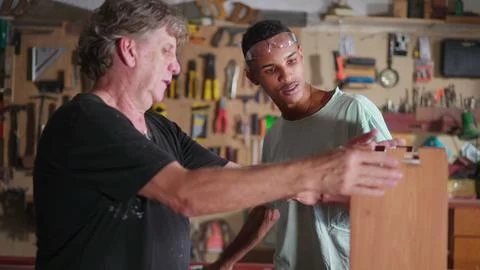 Senior carpenter guiding young apprentice to build craftmanship furniture a.. Stock Photos