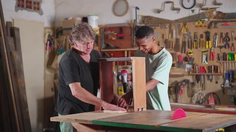 Senior carpenter guiding younger apprentice at carpentry workshop. Job occu.. Video stock 246767100