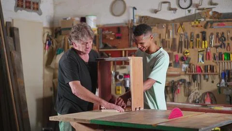 Senior carpenter guiding younger apprentice at carpentry workshop. Job occu.. Stock Photos