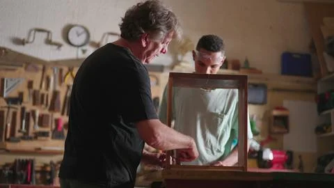 Senior carpenter at work with young apprentice, candid scene of carpentry w.. 库存照片