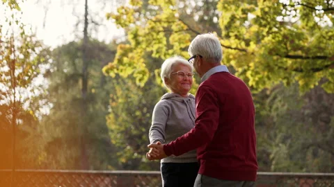 Senior caucasian couple slowly dancing in the park, smiling at each other, and Stock Footage