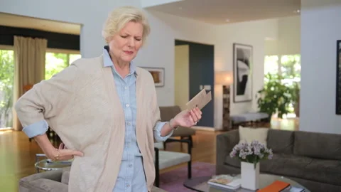 A senior Caucasian woman designing her living room, feels a pain in her back and Stock Footage