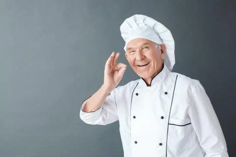 Senior chef studio standing isolated on gray showing ok gesture smiling happy Stock Photos