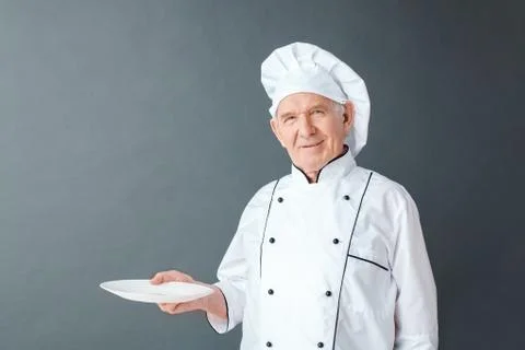 Senior chef studio standing isolated on gray with empty plate looking camera Stock Photos