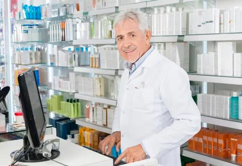 Senior Chemist Using Computer At Counter In Pharmacy 写真素材